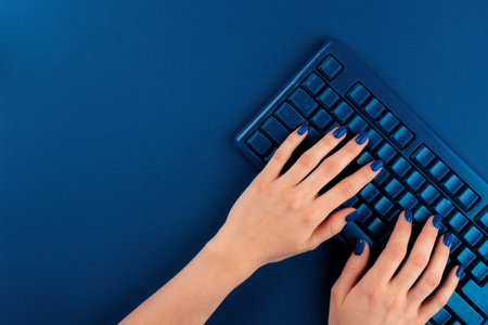 Woman hands typing on computer keyboard on classic blue backgroundの写真素材