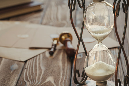 Wooden desk with vintage sandglass and old letter
