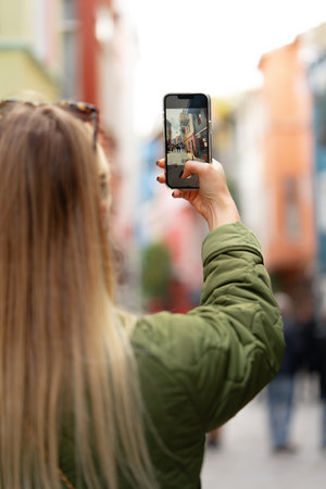 Woman taking photo with phone in the street back view