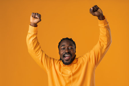 Portrait of excited african guy celebrating success with clenched fists against yellow backgroundの写真素材