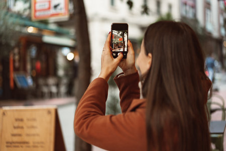 Brunette girl walking in the city and photographing by mobile phoneの写真素材