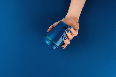 Female hand holding takeaway coffee cup gainst classic blue backgroundの写真素材
