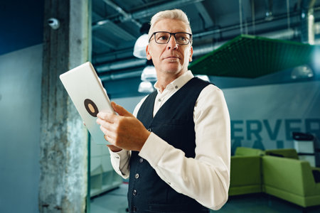 Handsome mature businessman using his digital tablet in the officeの写真素材