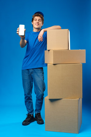 Young delivery man showing smartphone with blank screen in studioの写真素材