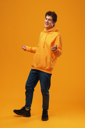 Young cheerful man dancing having fun over yellow backgroundの写真素材