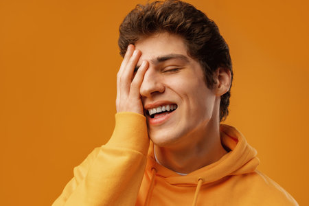 Young man wearing casual yellow hoody puts hand on face facepalm mistaken on yellow backgroundの写真素材