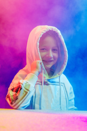 A little smiling girl in a hoodie stands in the colored smoke and looks at the cameraの写真素材