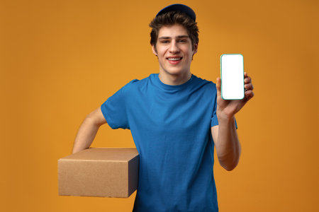 Young delivery man showing smartphone with blank screen in studioの写真素材