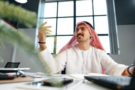 Young muslim businessman in traditional outfit working at the table in officeの写真素材