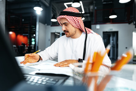 Young muslim businessman in traditional outfit working at the table in officeの写真素材