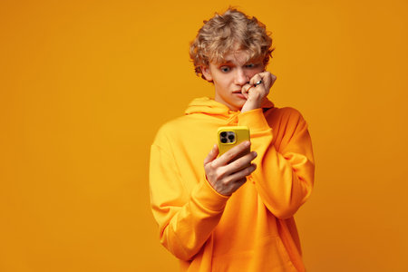 Happy caucasian young man using smartphone against yellow background