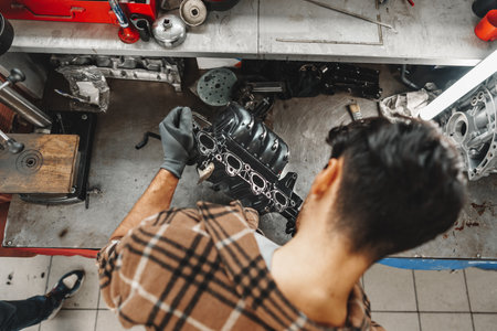 Young man mechanic repairing car parts on worktable in car service shopの写真素材