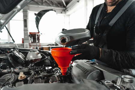 Close up of car service worker pouring new oil into car engineの写真素材