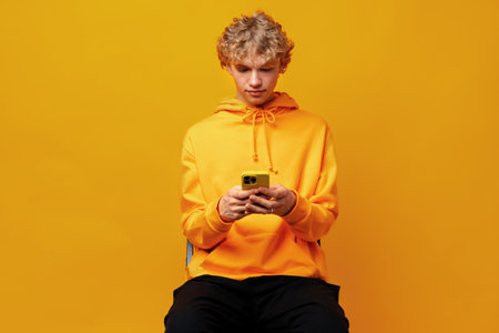 Happy caucasian young man using smartphone against yellow backgroundの写真素材