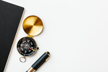 Black notepad for nautical notes and golden compass on a white tableの写真素材