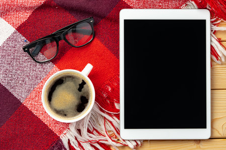 Top view of digital tablet with cup of coffee and glasses on plaid backgroundの写真素材