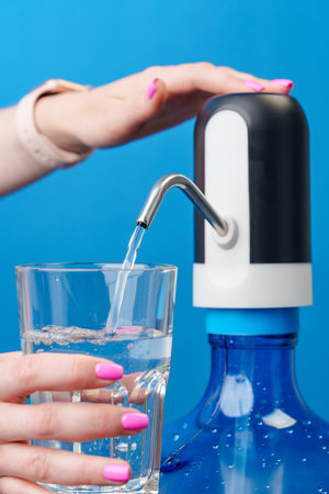 Womans hands pouring water into a glass from water cooler on blue backgroundの写真素材