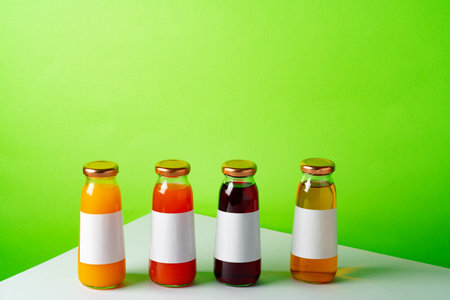 Glass bottles with juice on white table against green backgroundの写真素材
