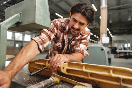 Young carpenter working on woodworking machines in the furniture factory