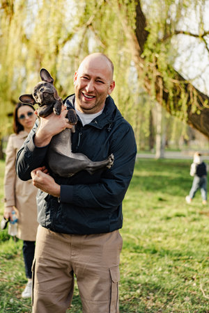 Man holding his french bulldog puppy in hands while having a walk in the parkの写真素材