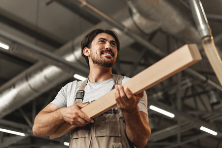 Young carpenter man looking and choosing wood plank at workshop in carpenter wood factoryの写真素材