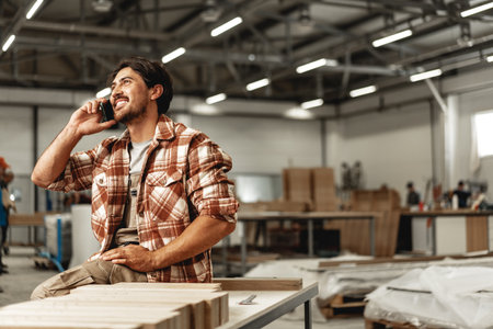 Young carpenter using his mobile phone in workshopの写真素材