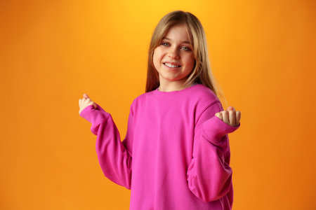 Portrait of a joyful happy teenage girl celebrating success on yellow background