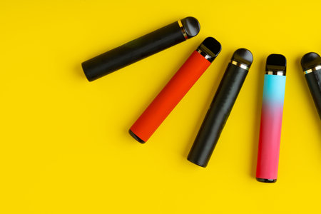 Colorful disposable electronic cigarettes on yellow background