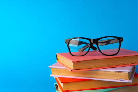 Reading glasses on stacked books against blue background