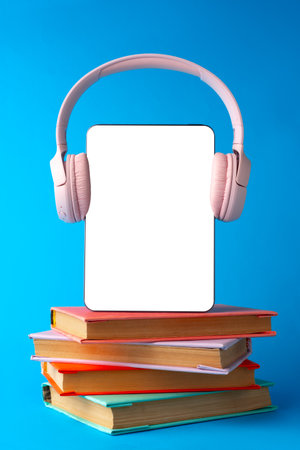 Stacked books with digital tablet and headphones against blue backgroundの写真素材
