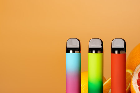 Three electronic cigarettes with citrus fruits on orange backgroundの写真素材