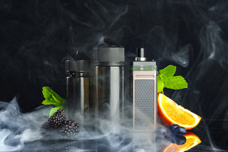 Vape and smoking liquid with fruit against black background with smokeの写真素材