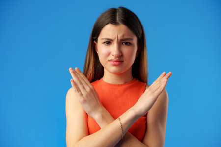 Teen girl shows cross hands gesture, rejecting something over blue background in studio