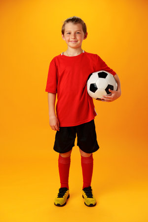 Teen boy soccer player with football ball against yellow backgroundの写真素材