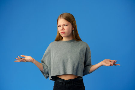 Puzzled teen girl dont know what to do on blue background in studio