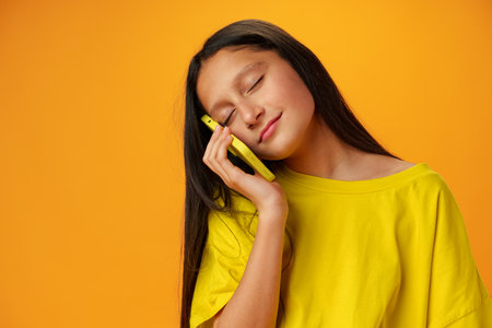 Teen girl over yellow wall talking on smartphoneの写真素材
