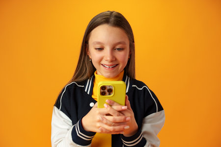 Stylish teen girl using smartphone over yellow background in studio