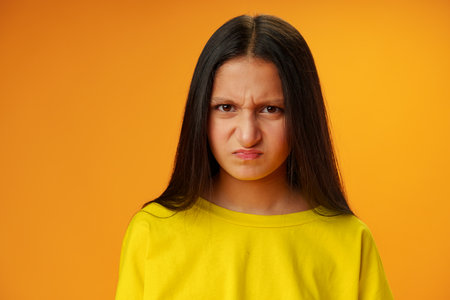 Angry dissatisfied teen girl against yellow background