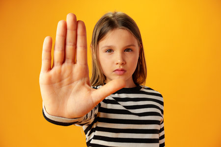 Teen girl extend hand in block gesture against yellow backgroundの写真素材