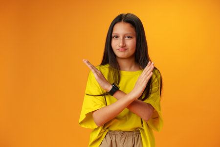 Teen girl shows cross hands gesture, rejecting something over yellow background in studioの写真素材