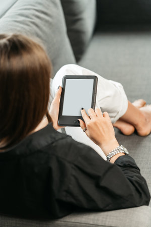 Young woman sitting the couch with an e-bookの写真素材