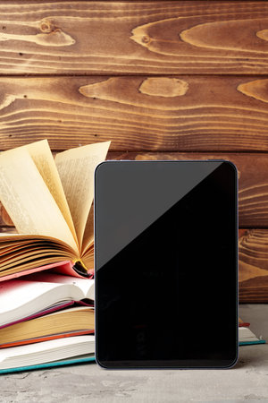 Digital tablet and stack of hardcover books against wooden backgroundの写真素材