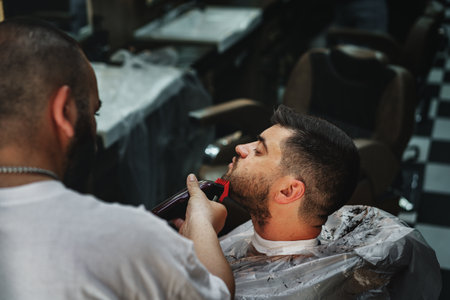 ISTANBUL, TURKEY - MAY 16, 2022: Hairstylist doing beard haircut for male client in barbershop in...