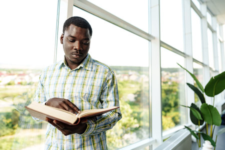 African man standing near the window in room and reading a bookの写真素材