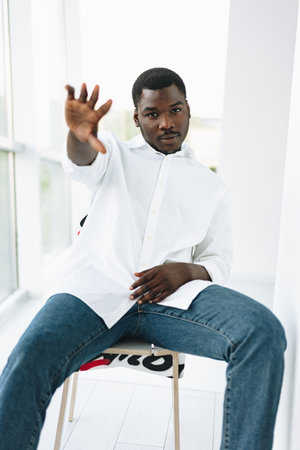 Young african man in white shirt and glasses posing near large windowの写真素材