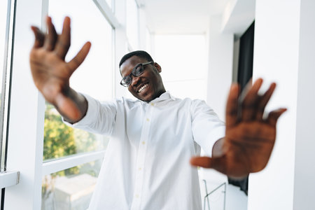 Young african man in white shirt and glasses posing near large windowの写真素材