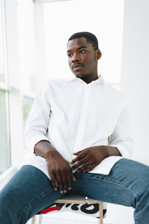 Young african man in white shirt and glasses posing near large windowの写真素材