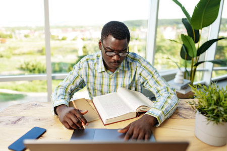 Serious concentrated african man studying or working with laptop indoorsの写真素材