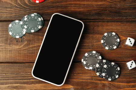 Poker chips and smartphone on wooden table