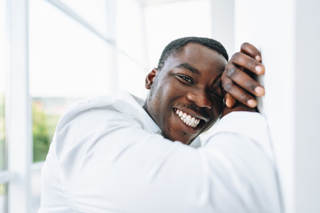 Young african man in white shirt and glasses posing near large windowの写真素材